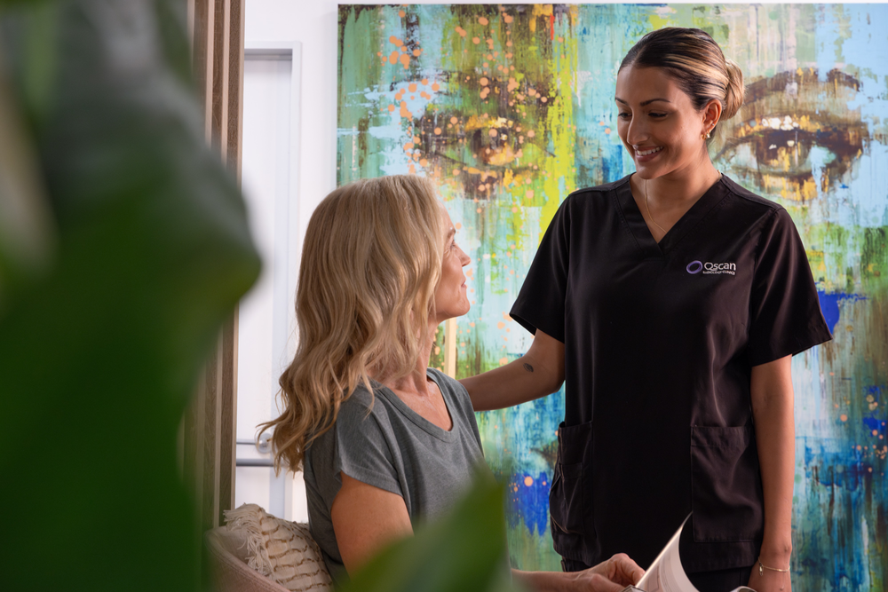Qscan radiographer speaking with a smiling patient seated in reception prior to her appointment. 