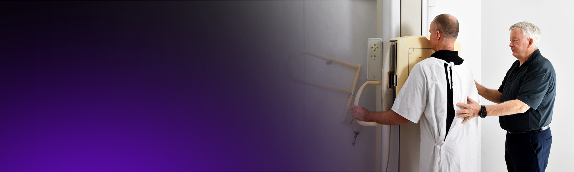 A male radiographer positions a male patient for a chest x-ray.